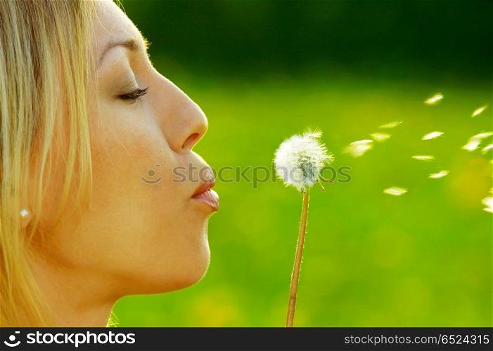 The girl blows on a dandelion on a background of a grass. Spring entertainments