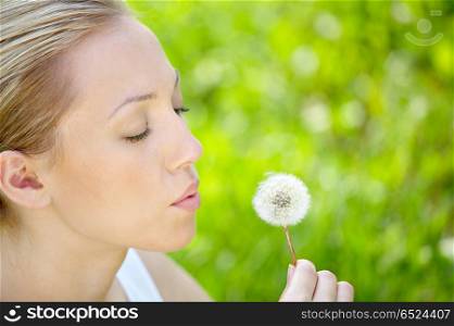 The girl blows on a dandelion on a background of a grass. Spring entertainments