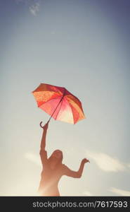 The girl dances with an umbrella in her hands against the clear sky, the picture is tinted in retro colors and a vignette is added. The girl dances with umbrellas in her hands against the clear sky, the picture is tinted in retro colors