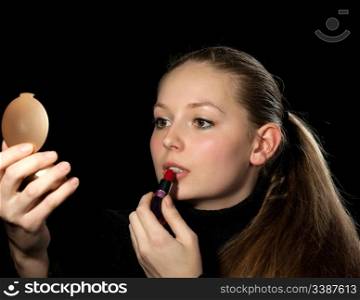 The girl does a make-up before a mirror. On a black background
