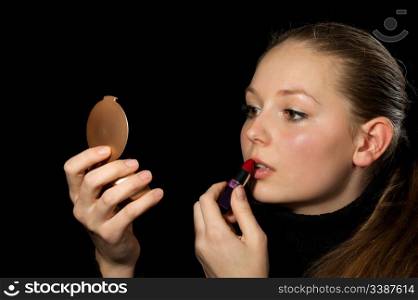 The girl does a make-up before a mirror. On a black background