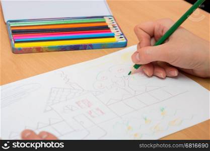 The girl draws a picture with colored pencils on paper, close-up
