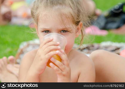The girl drinks juice from a plastic disposable cup on a picnic
