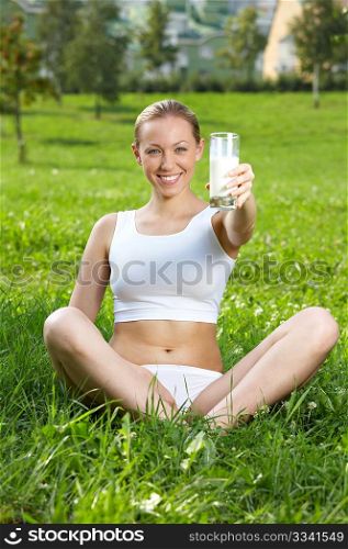 The girl holds in a hand a glass with milk against a lawn
