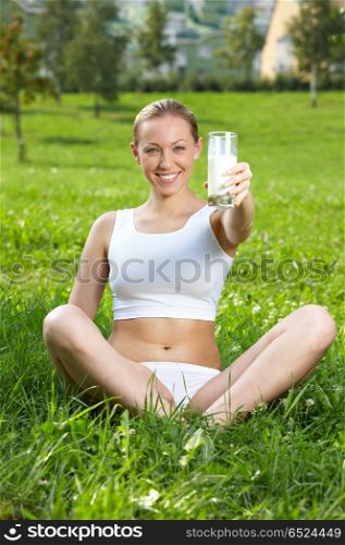 The girl holds in a hand a glass with milk against a lawn. Idea for health