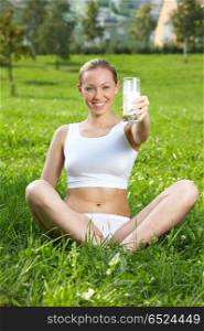 The girl holds in a hand a glass with milk against a lawn. Idea for health