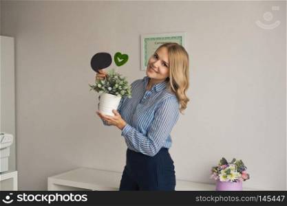 The girl in front of a white wall holding a pot of flowers and a sign.. Girl holding a pot of flowers 9025.