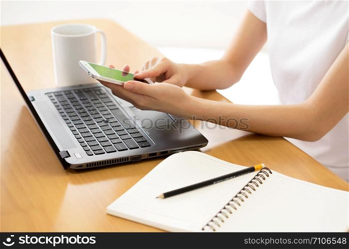 The girl in the hands holding a mobile phone. Laptop with blank notepad and pencil with sheets paper