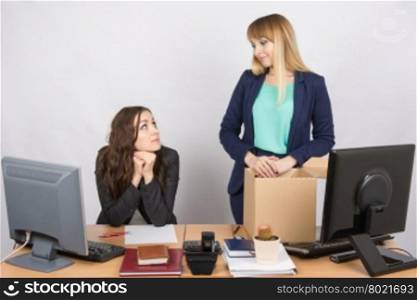 The girl in the office is facing the box with things and looking at the colleague sitting next
