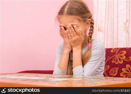 The girl is crying covering his face with his hands collecting picture of puzzles