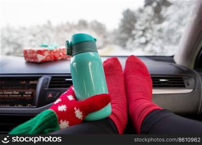 The girl is holding a thermos while sitting in the car in winter, on the background of the winter forest. Travel, trip and winter concept. The girl is holding a thermos while sitting in the car in winter, on the background of the winter forest. Travel, trip and winter concept.