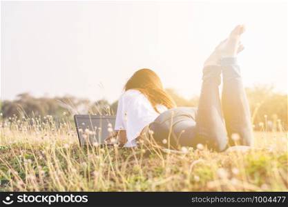 The girl is lying down using a laptop in the park with the sun in the morning.