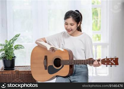 The girl is sitting and playing the guitar on the chair.