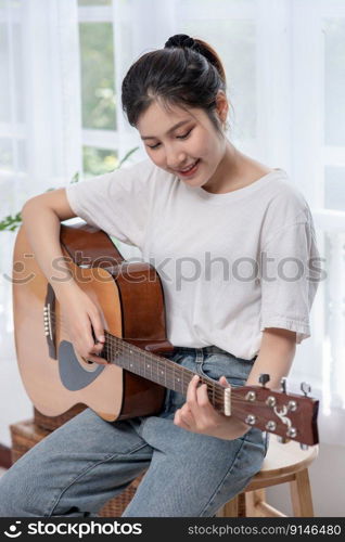 The girl is sitting and playing the guitar on the chair.