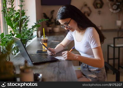 the girl is sitting in a cafe at the bar, looking at the phone, holding glasses in her hand, a lapto.. the girl is sitting in a cafe at the bar, looking at the phone, holding glasses in her hand, a lapto