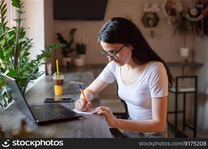 the girl is sitting in a cafe at the bar, looking at the phone, holding glasses in her hand, a lapto.. the girl is sitting in a cafe at the bar, looking at the phone, holding glasses in her hand, a lapto