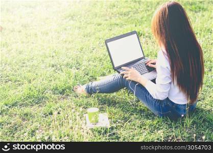 The girl is using a laptop in a green field with a morning sunshine, mock up, vintage tone.