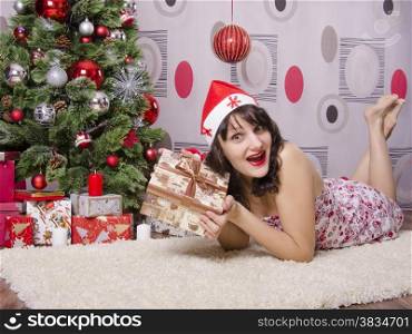 The girl lying on the carpet around the Christmas tree. In her hands a big box with a present. The girl joyfully looking in the frame