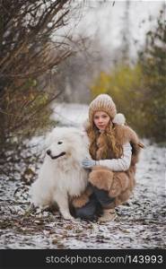 The girl petting the dog on the walk in the late autumn.. A child hugging and petting his white shaggy dog Samoyed 9855.