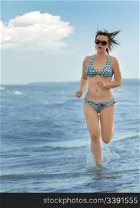 The girl running on seacoast. The European appearance in sunglasses