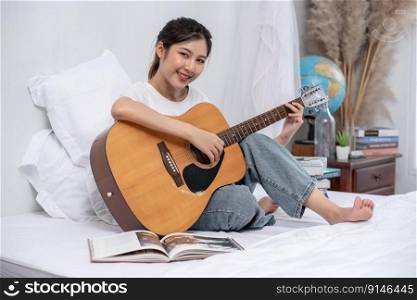 The girl sat and played the guitar on the bed.