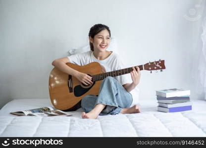 The girl sat and played the guitar on the bed.