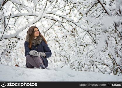 The girl sat down in a beautiful snowy forest and admires the beauty