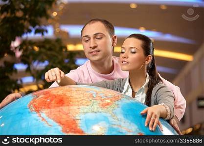 The girl shows to the guy a place on the big copy of globe