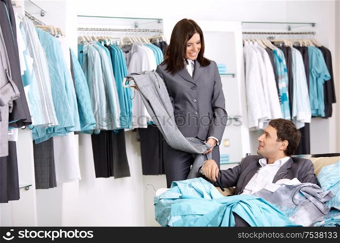 The girl shows to the man trousers chosen in shop