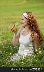 The girl sits on a background of a green lawn and drinks juice. Rest in park