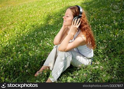 The girl sits on a meadow and listens to music in ear-phones