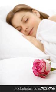 The girl sleeps in bed, nearby there is a rose, isolated