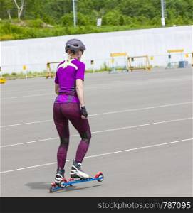The girl sportswoman rides on the roller skis on the asphalt
