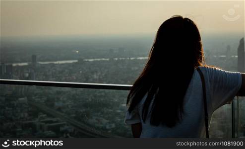 the girl stood on the roof of the building looking at the city full of dust and air pollution and the sunrise background evening time Bangkok Thailand