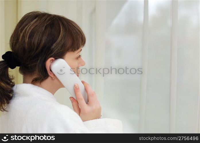 The girl talking by phone. After morning douche in a white dressing gown