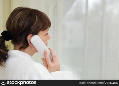 The girl talking by phone. After morning douche in a white dressing gown