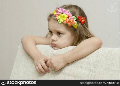 The girl thoughtfully looks to the left, his arms dangling from the back of the couch, and laid on the sofa his head. On the head of a girls band with beautiful flowers