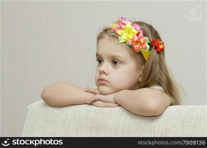 The girl thoughtfully looks to the left, his arms dangling from the back of the couch, and laid on the sofa his head. On the head of a girls band with beautiful flowers