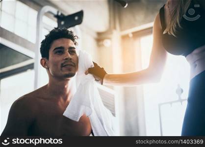 The girl uses a handkerchief to sweat the young man while exercising in the gym.