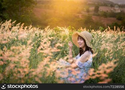 The girl wearing a hat, wearing a white dress, sit in the middle of the grass with beautiful white flowers with a relaxed and happy mood on mountain in sun set time.