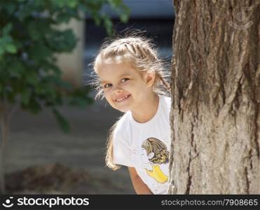 The girl with a smile peeked out from behind a tree on the left side