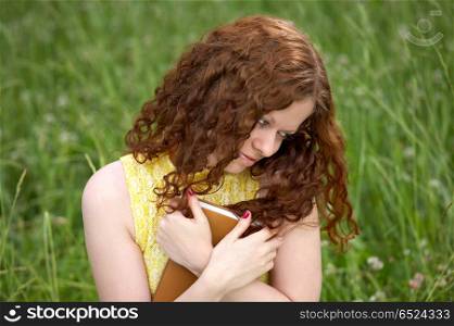 The girl with long hair presses to a breast the book on a background of a lawn. Leisure with reading