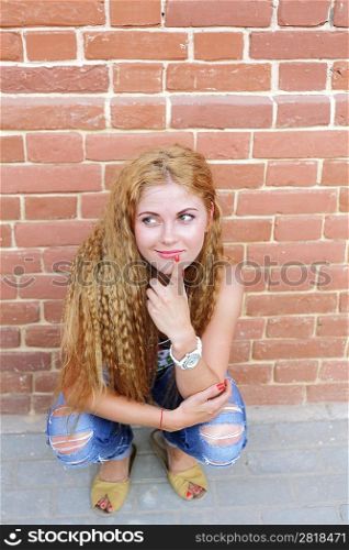 The girl with long hair sitting near wall looking playfully