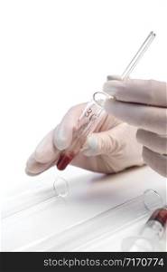 the gloved hand of a laboratory assistant holds a test tube with a blood sample on a white background. also in the photo is a syringe with a blood sample