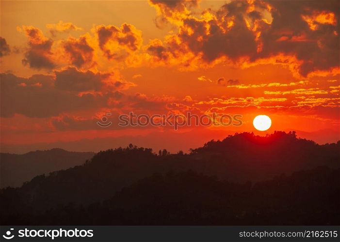 The glowing sun setting over mountains range near Thailand-Myanmar border. Dramatic clouds in the sunset sky. Silhouette.