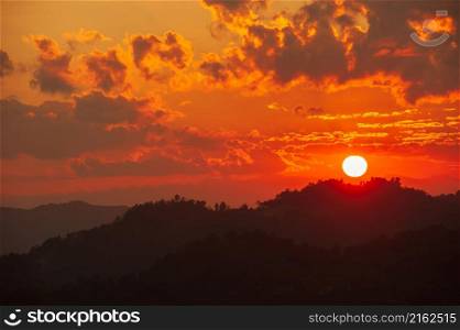 The glowing sun setting over mountains range near Thailand-Myanmar border. Dramatic clouds in the sunset sky. Silhouette.