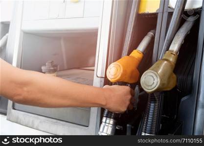 The gold car is filling the fuel at the oil station. Hand holding Fuel nozzle in gas pump.