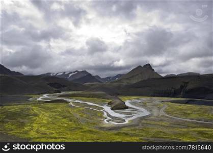 The green river bedding amongst the volcanic mountain ridges in the Landmannalaugar region Iceland on an overcast day