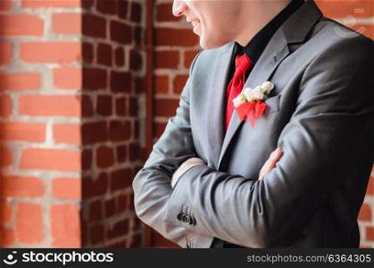 the groom at the window in a dark suit and red tie against a brick wall