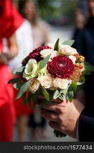The groom brings a bouquet for the bride. Groom with bridal bouquet of roses, berries and dahlias